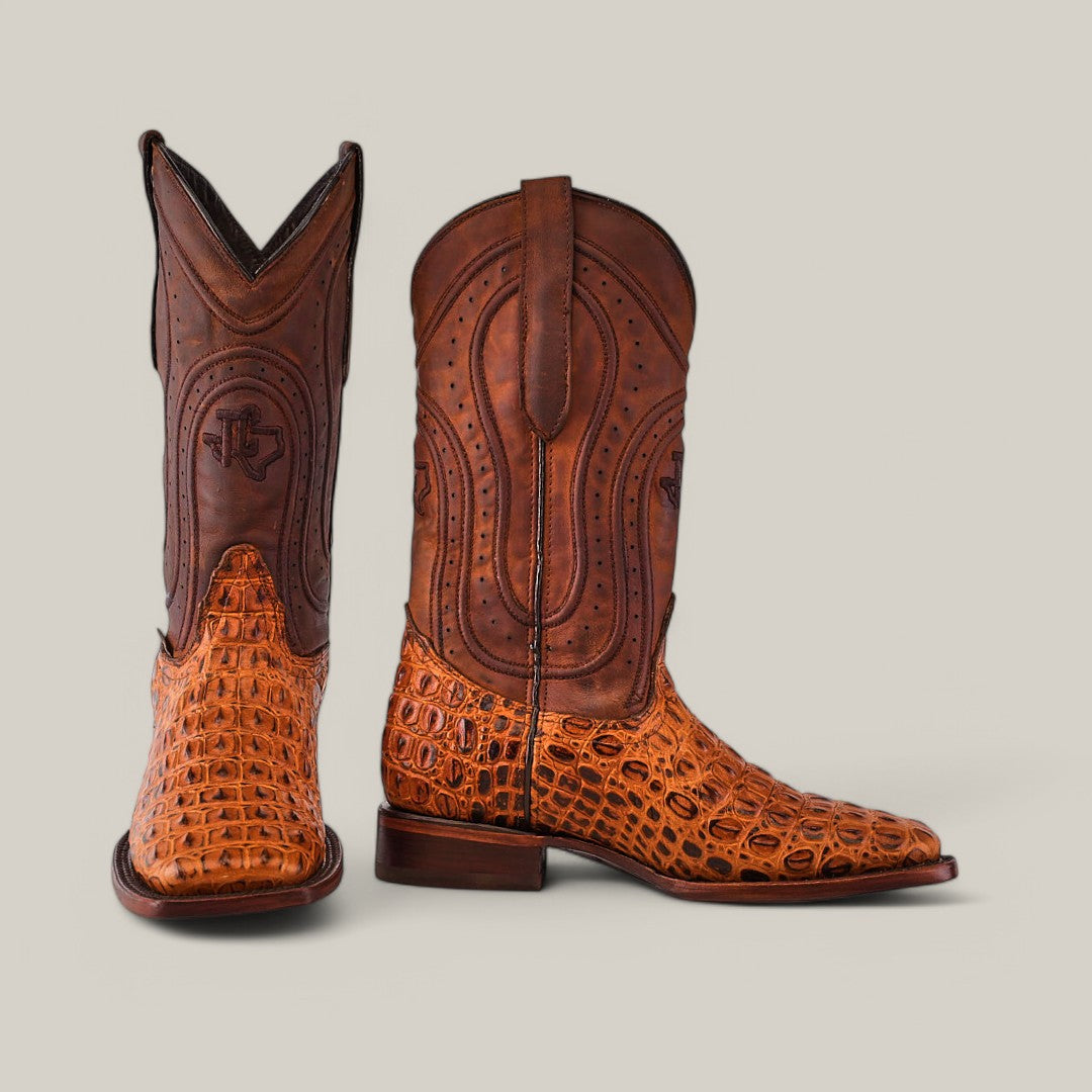 The Alligatoar Horn Back Print Honey cowboy boots feature brown leather with a square toe and intricate stitching. The alligator horn back print gives a unique texture, shown in side and front views against a light gray background.