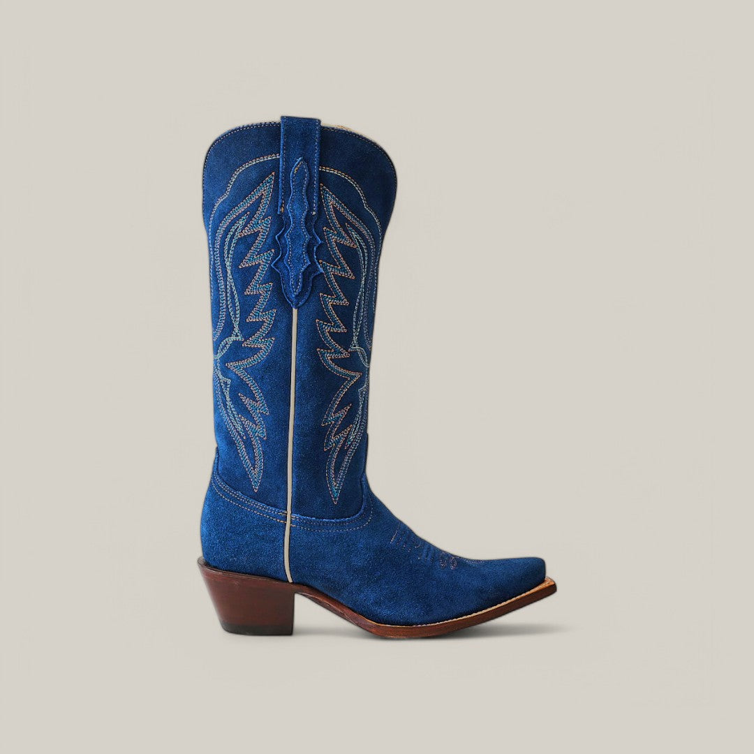 The Miranda Suede Blue Jeans boot features decorative stitching, a snip toe, and a brown angled heel. This suede masterpiece boasts a sleek leather sole and is displayed against a plain light gray background.