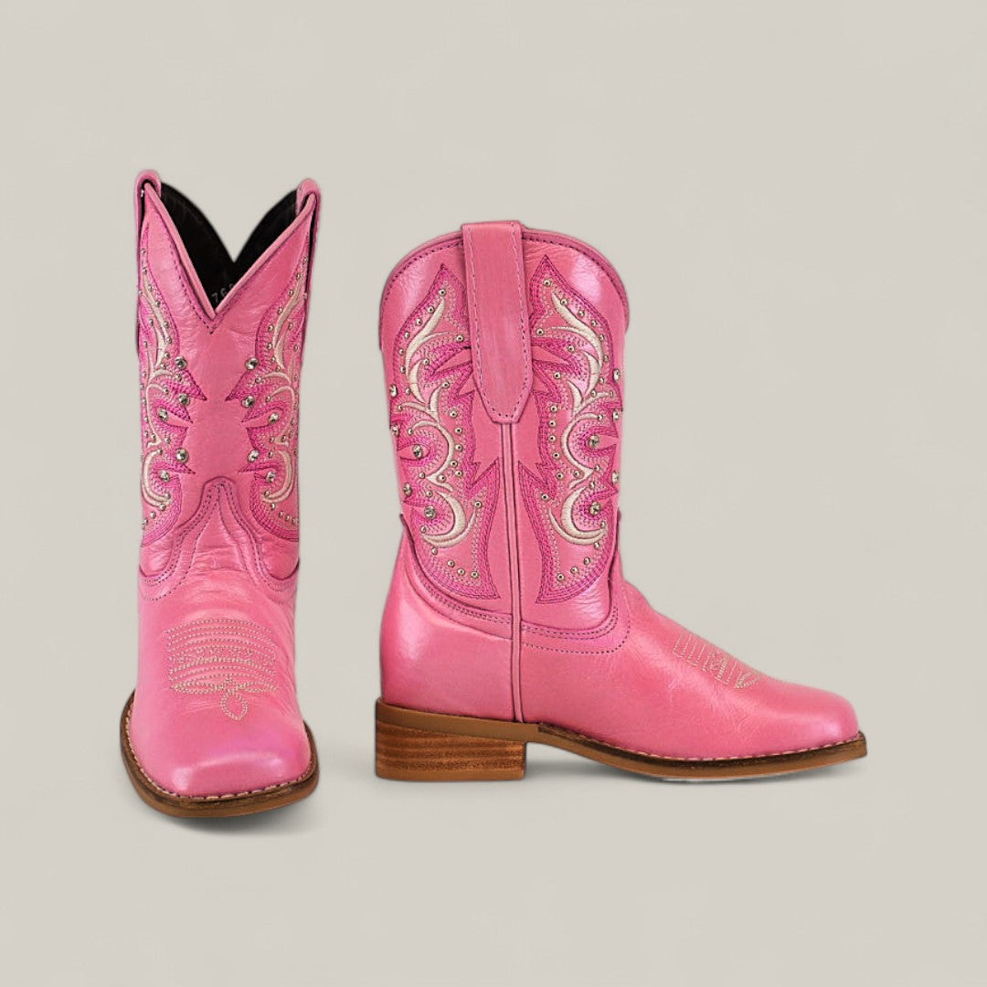 The Amara Pink - Square Toe - Kids Boots feature bright pink color, decorative stitching, low brown heel, and light-colored sole. One boot is shown front-facing, the other from the side. Available in childrens sizes.