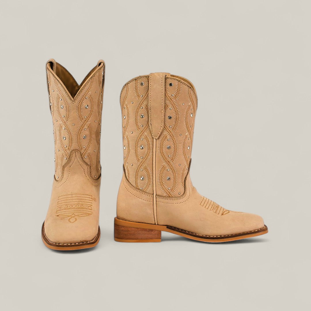 The Premiere Suede Bone - Square Toe Kids boots feature premium tan suede, decorative stitching, and silver stud accents; one boot stands upright while the other is shown in side profile against a plain light background.