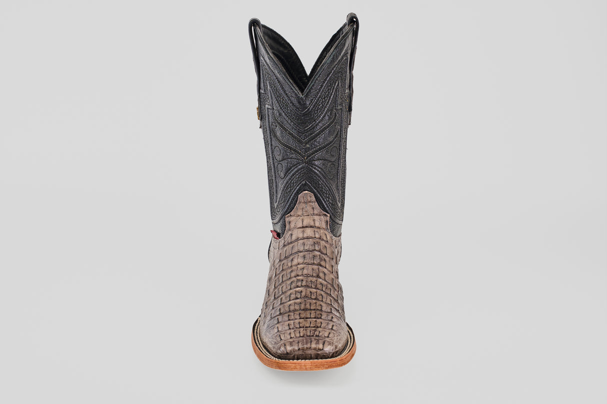 The Exotic Caiman Horn Back - Serpentine - Square Toe boot is shown from the front, displaying a textured reptile-like lower, dark stitched shaft, and light brown sole—a classic western look against a plain background.