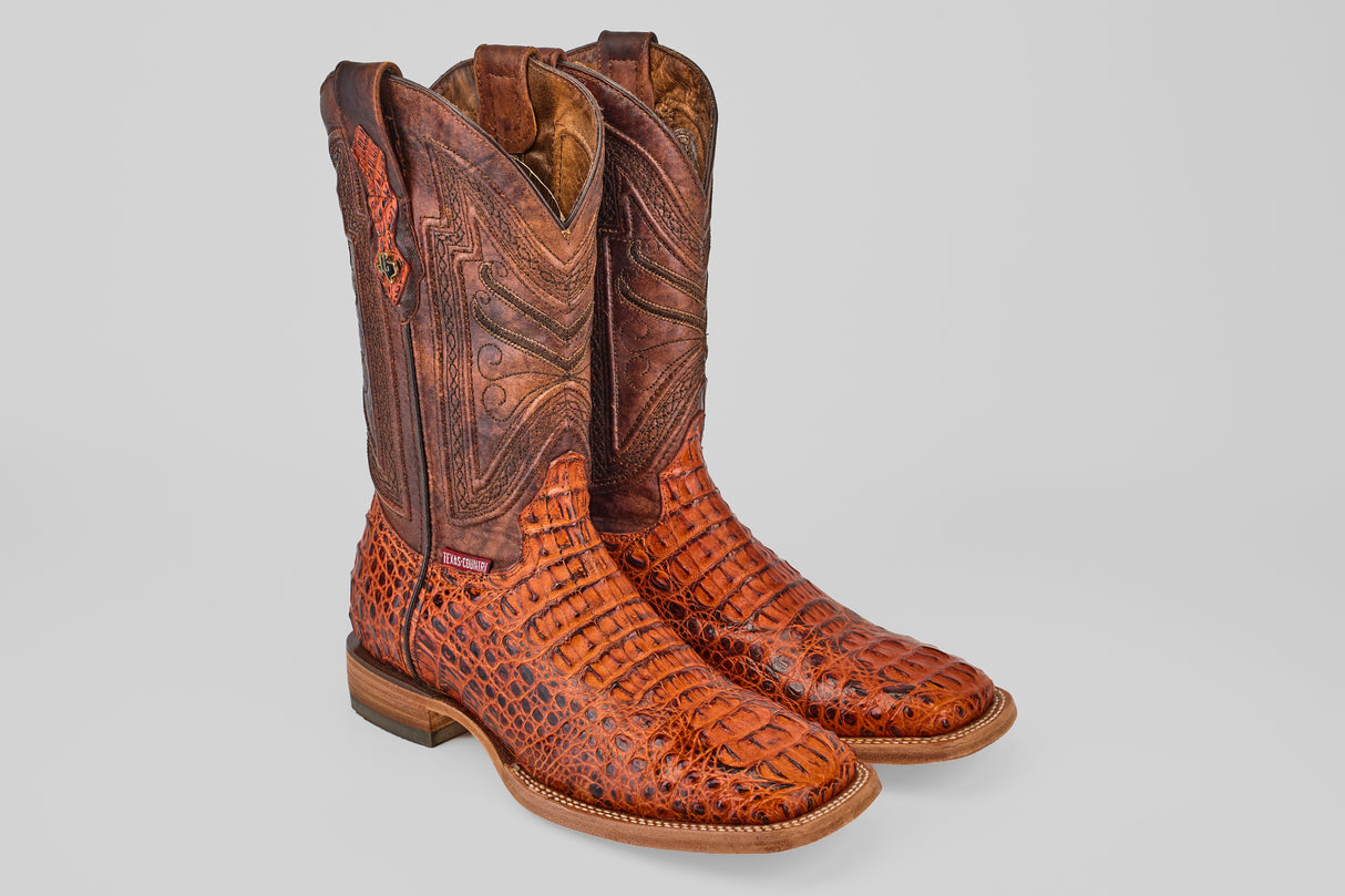 A pair of Exotic Caiman Head - Cogñac - Square Toe boots with patterned, textured caiman leather and decorative stitching on the tall shafts, displayed against a plain light gray background.