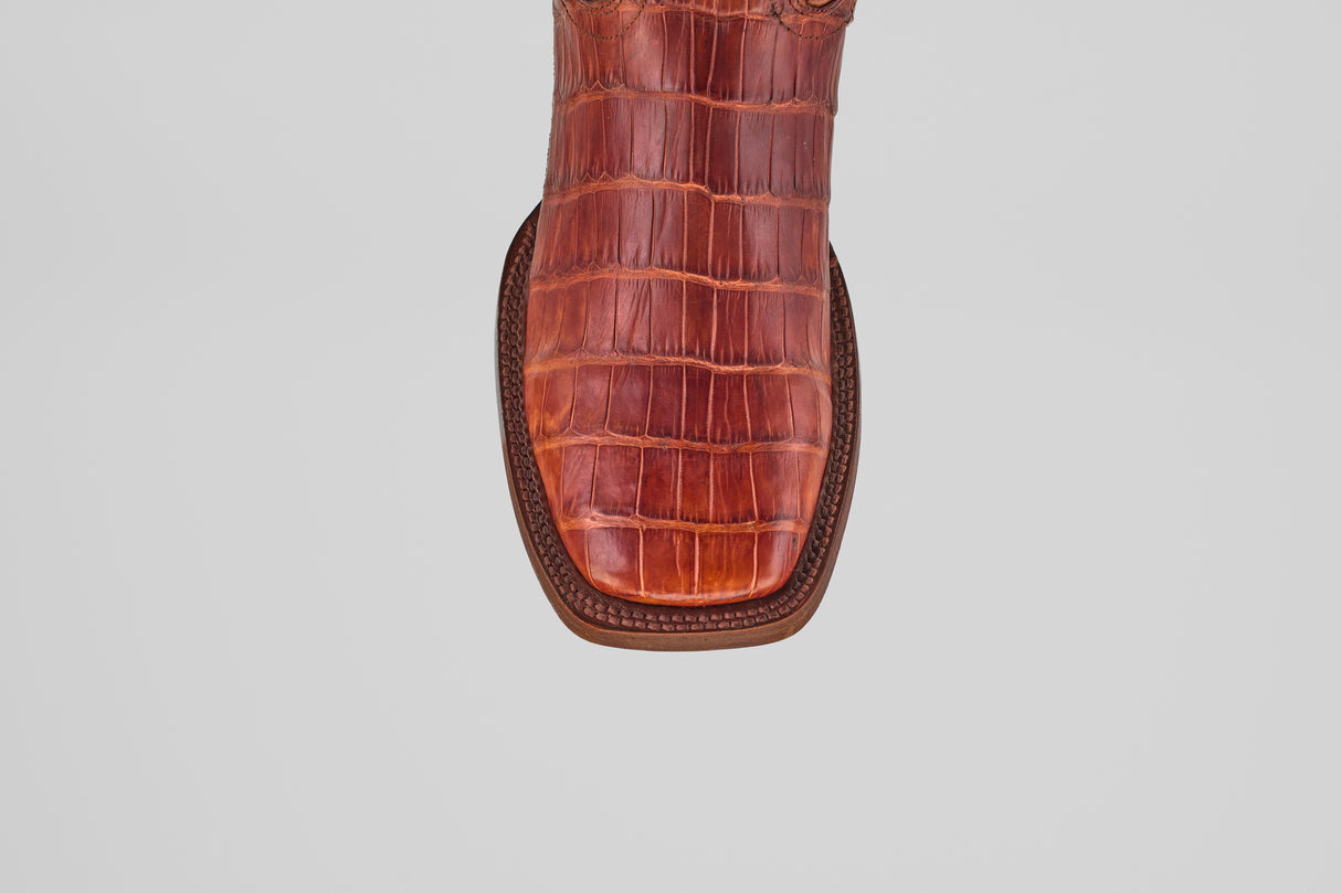 A close-up, top-down view of the Exotic Alligator Tail - Brick - Square Toe boot’s reddish-brown, square toe with genuine alligator leather texture, displayed against a plain light gray background.