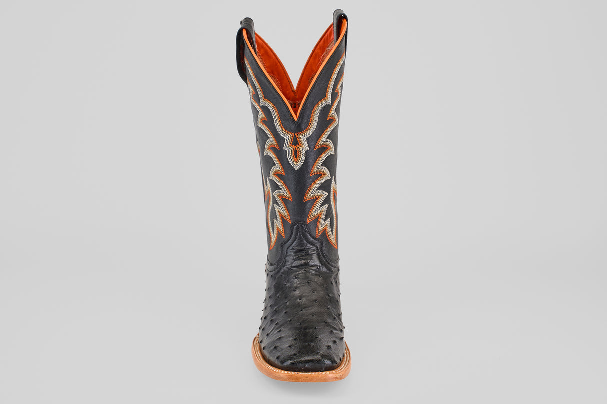 The Steele - Black - Square Toe boot features textured leather, a black square toe, intricate orange and grey stitching, and a brown sole, presented front view against a light gray background—ideal for luxury footwear seekers.