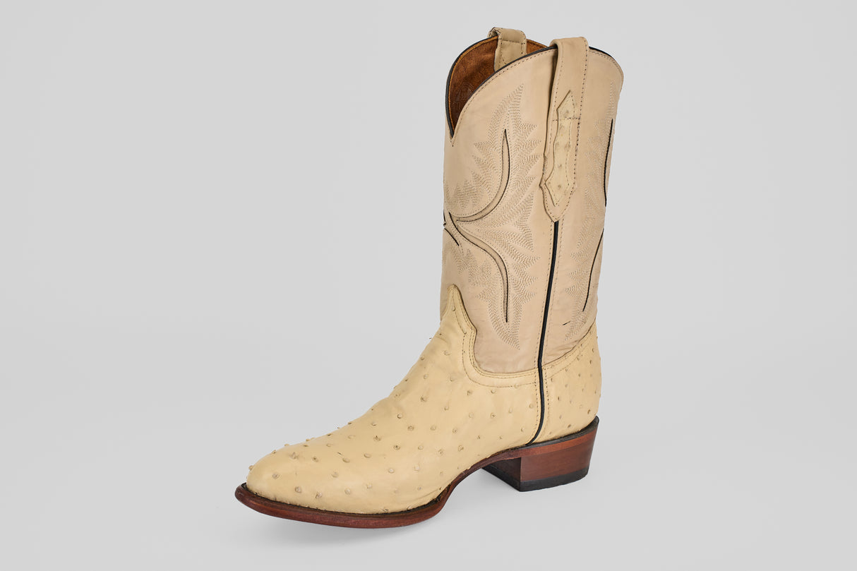 The Exotic Full Quilt Ostrich - Bone - Round Toe is a handcrafted light tan cowboy boot made from genuine ostrich leather, featuring decorative shaft stitching, brown heel, and side pull straps—shown against a plain white background.