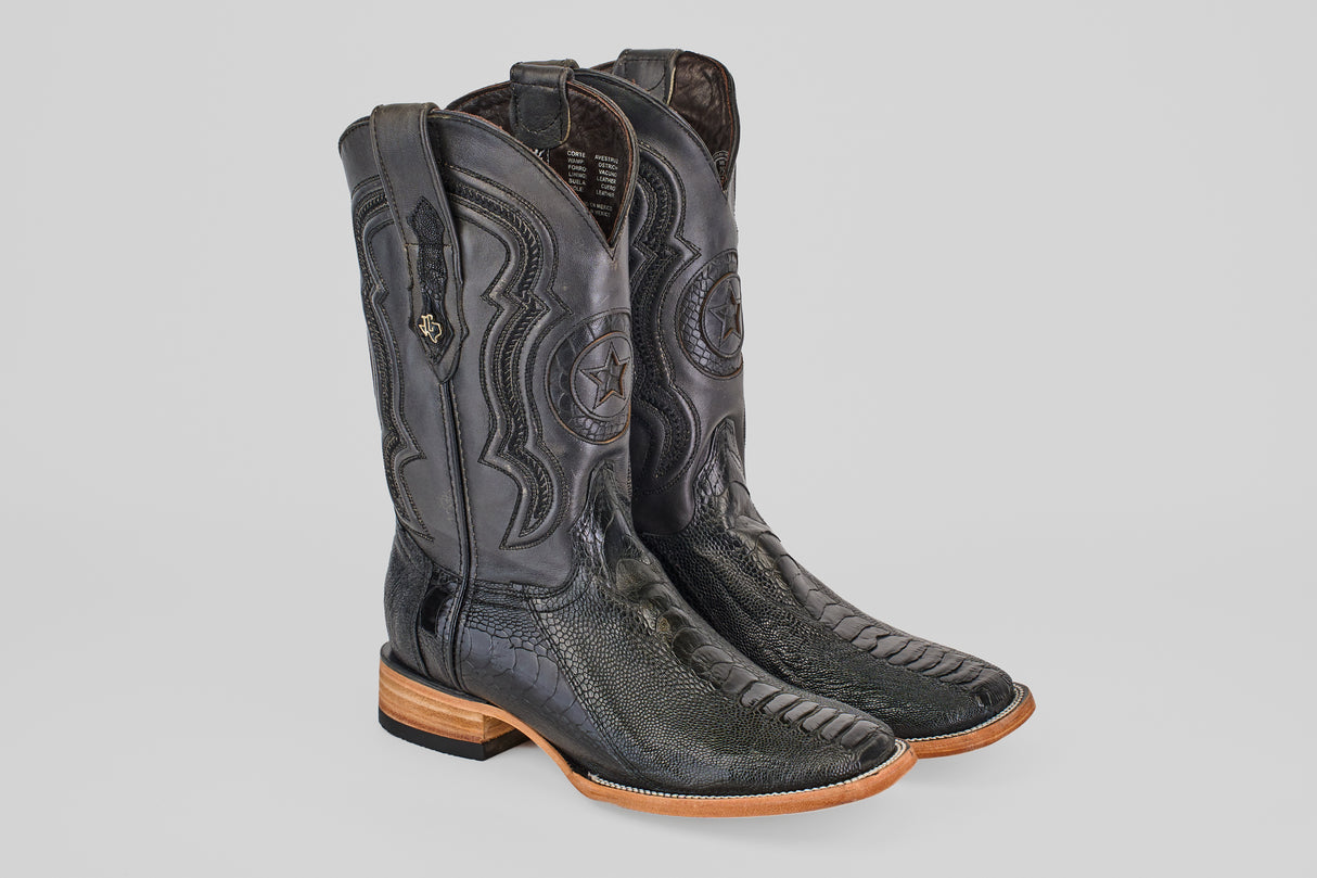 The Austin Leg - Black - Square Toe boots feature black ostrich leather, decorative stitching with a star design on the shaft, square toes, and light brown wooden soles, displayed on a light gray background.