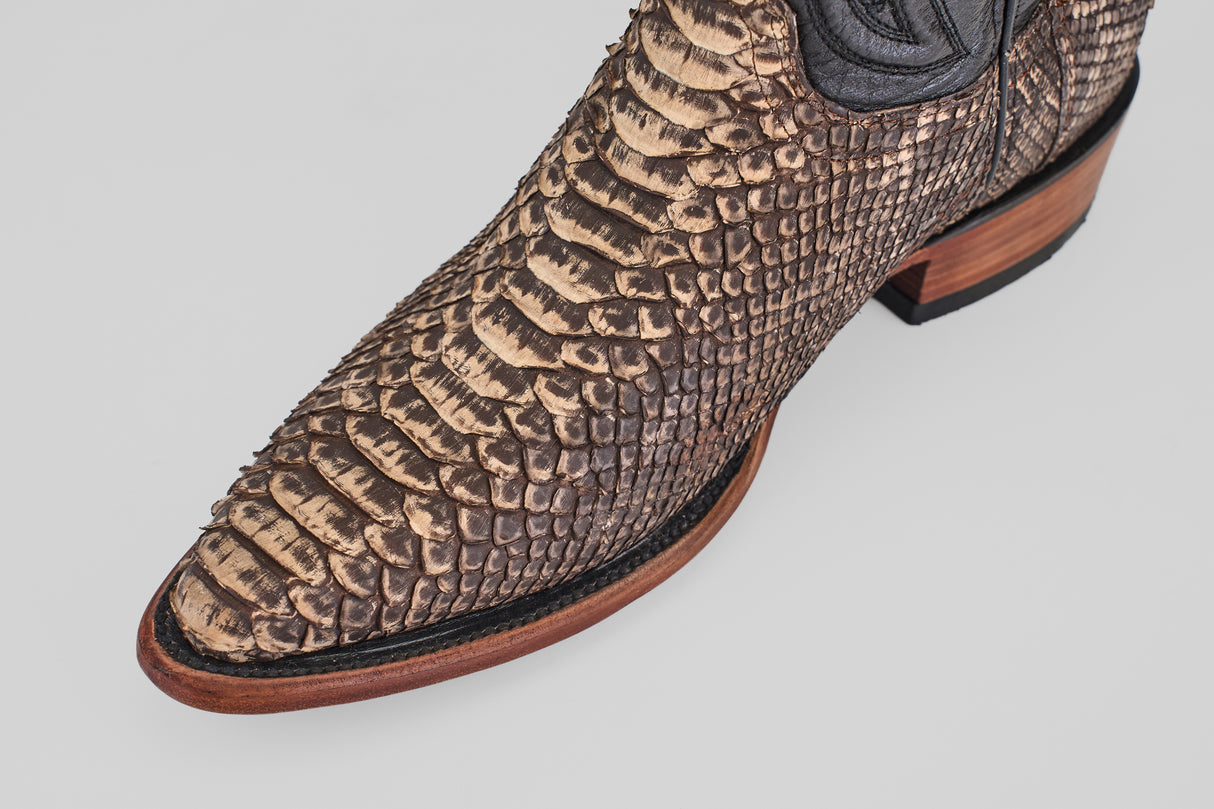 Close-up of the snip toe and upper of the Tanner – Rustic Bone boot, crafted from textured, patterned brown python leather with a wooden sole and black trim, set against a plain light background.