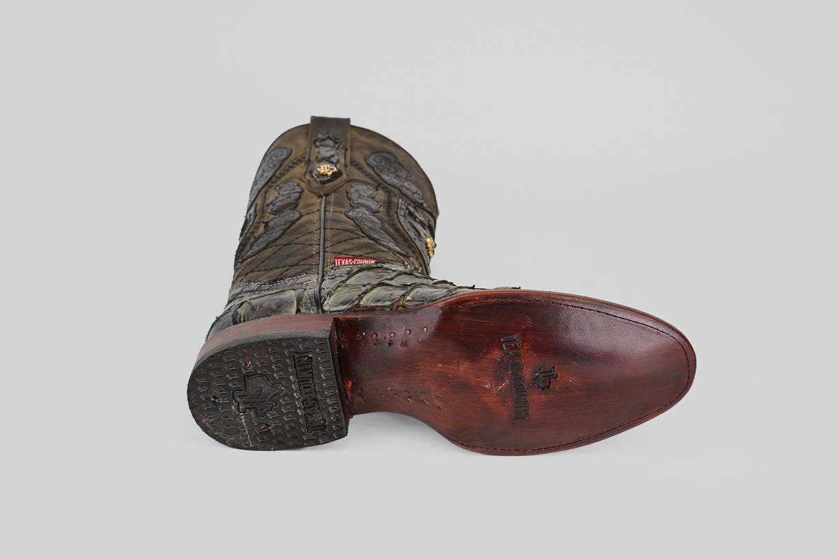 A single Conor - Charcoal - Roper Toe boot lies on its side, showcasing intricate upper stitching and a polished, reddish-brown fish leather sole with a decorative stamp and textured heel.