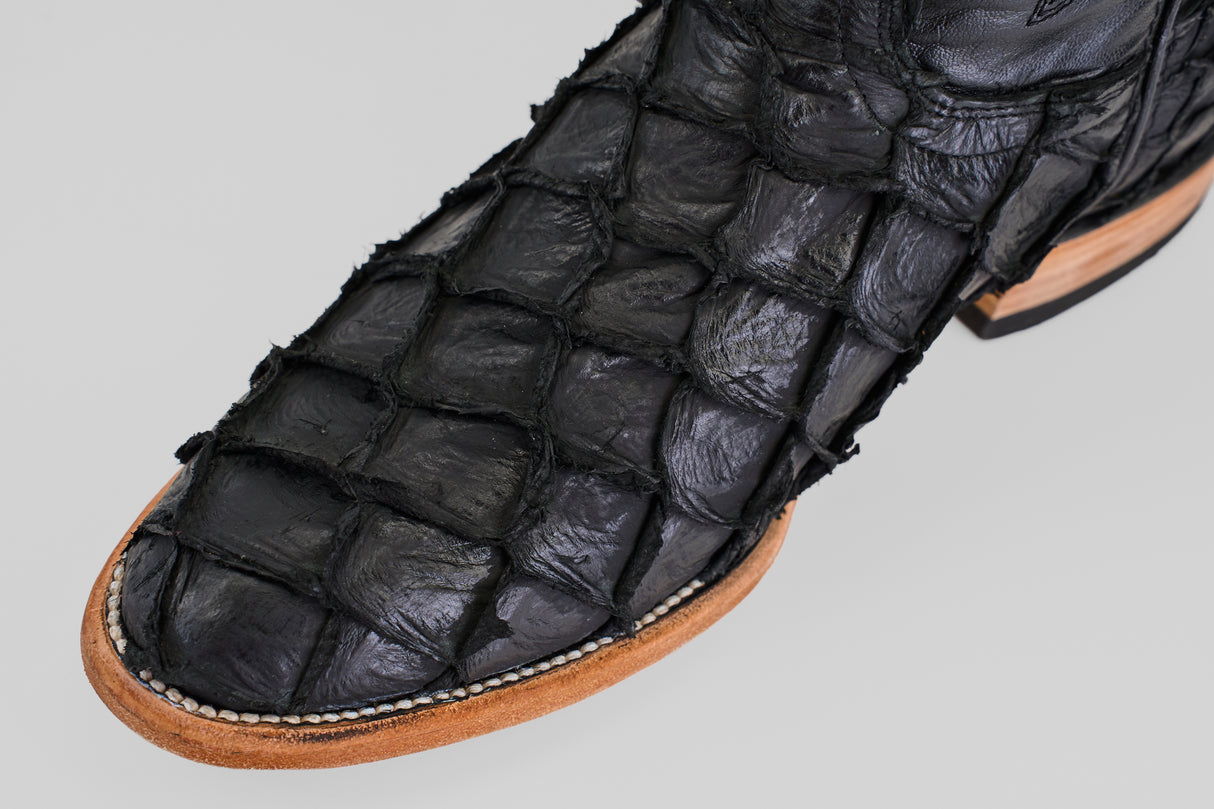 Close-up of the Conor - Matte Black - Roper Toe: a black boot with textured, square-patterned leather, light brown sole, and visible white stitching along the edge.