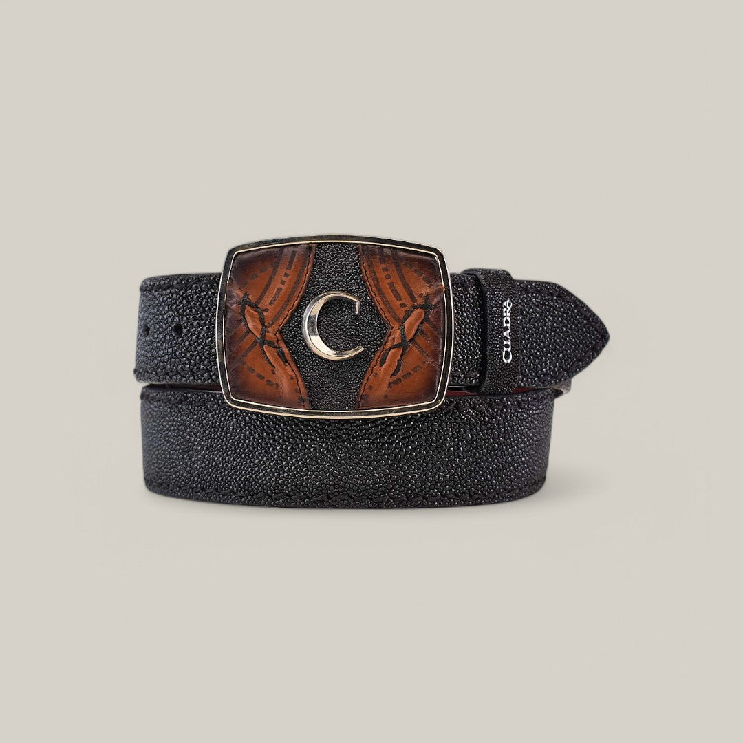The Black Stingray Laser Belt - BC350 features a subtle stingray texture and a large rectangular buckle with intricate brown leather details and a silver crescent emblem. Elegantly coiled on a plain gray background, it is the perfect stylish accessory.