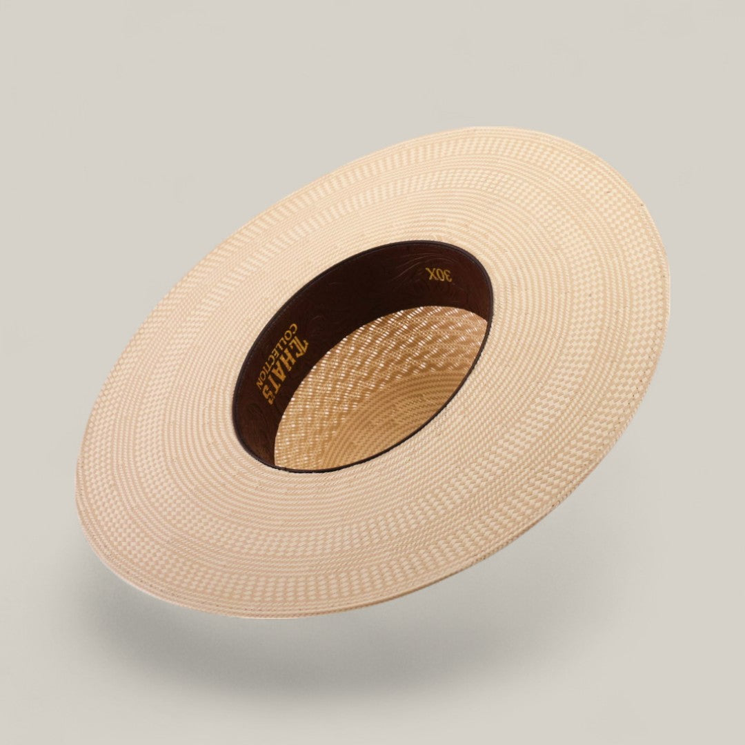 The 30X Worm - Open Crown is a wide-brimmed, light beige straw hat with a patterned weave and dark brown inner band with gold lettering, shown at an angle against a plain background—a unique choice for customizable hat styles.