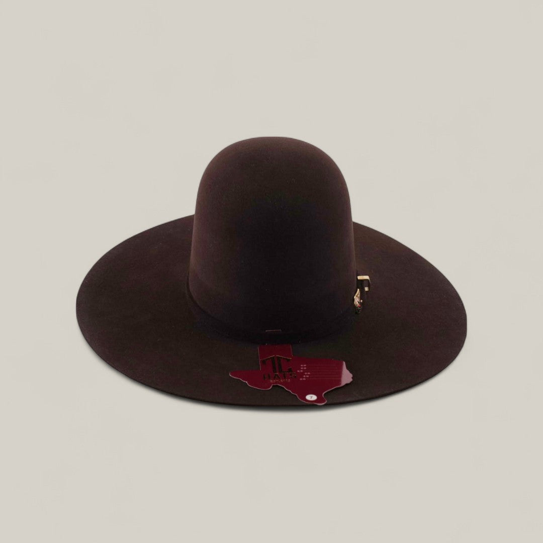 The 10X - Chocolate - TC Hats, a wide-brimmed dark brown Western hat with a decorative band and Texas-shaped tag on the brim, is displayed on a plain, light background.