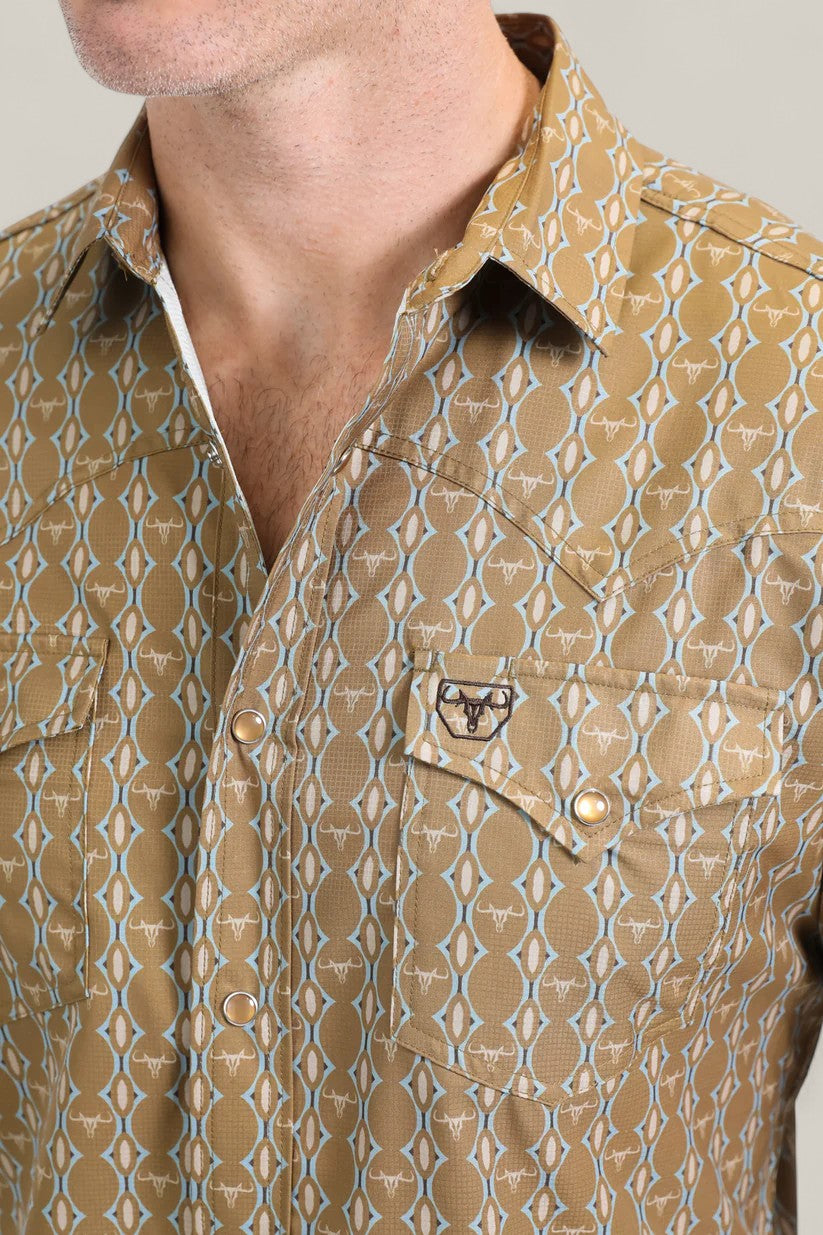 A close-up of a person wearing the Mens Performance Western Short Sleeve Aztec Print Camel Shirt (PGW10645), featuring white geometric designs, two chest pockets (one with an embroidered bull head), and a partially unbuttoned collar.