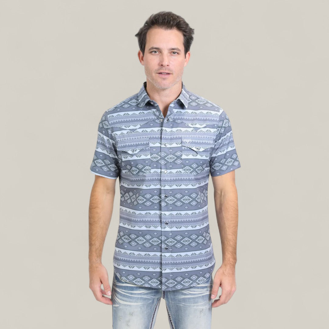 A man wearing the Mens Performance Western Short Sleeve Aztec Print Grey Shirt (PGW10649) faces forward against a plain light background, pairing it stylishly with faded blue jeans and sporting short dark hair.