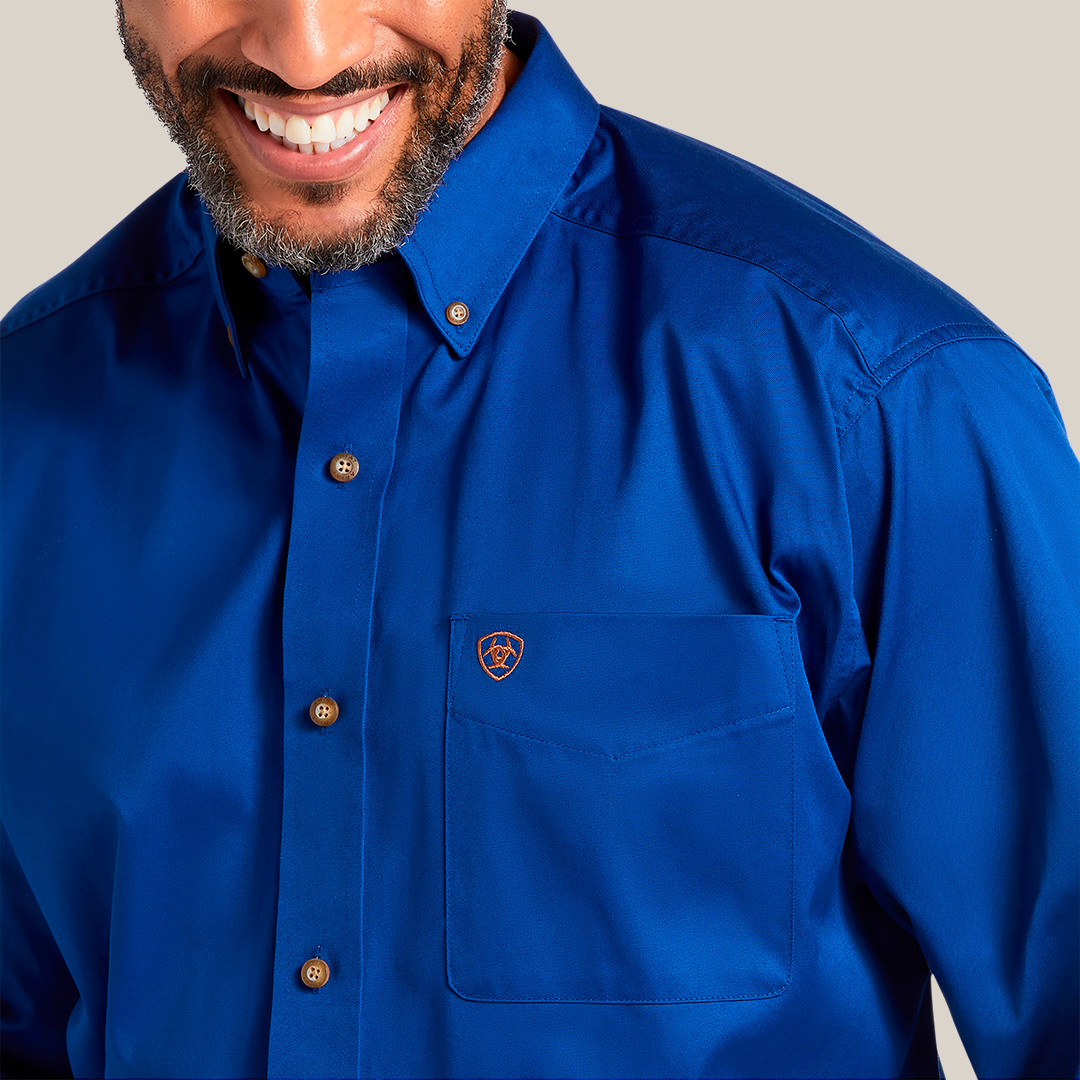 A person smiling in a Solid Twill Classic Fit Shirt Blue - 10006660, made of 100% cotton twill, with brown buttons and a small emblem on the pocket. The smart collar adds to its charm. Image highlights the upper chest and part of the face.