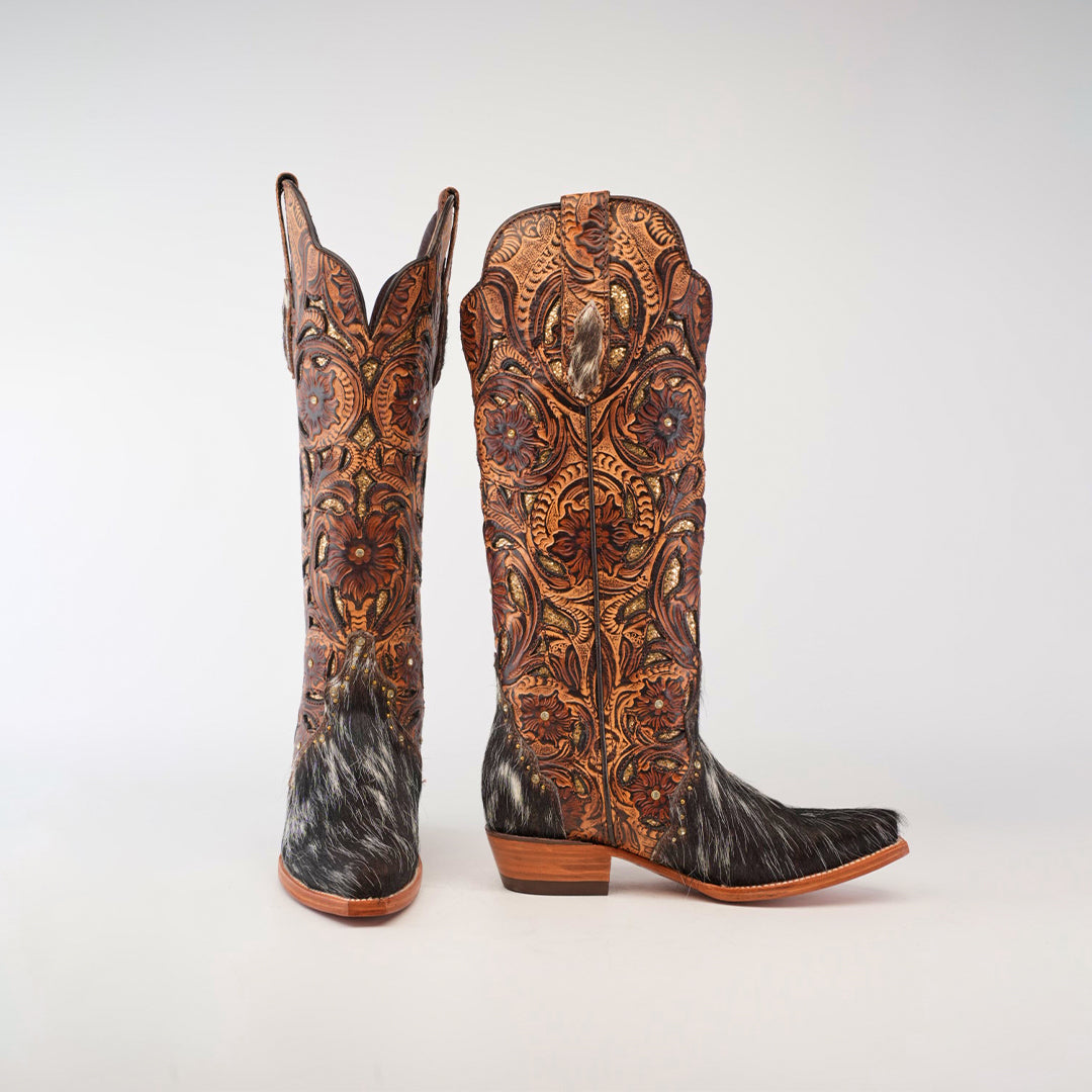 A pair of ornate western boots with intricate leather patterns and dark fur accents on the lower half, set against a plain background.