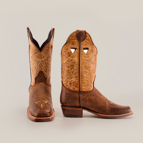 Two brown leather cowboy boots with intricate stitched patterns. One boot faces forward showing the toe design, and the other is turned to the side, highlighting the detailed upper embroidery.