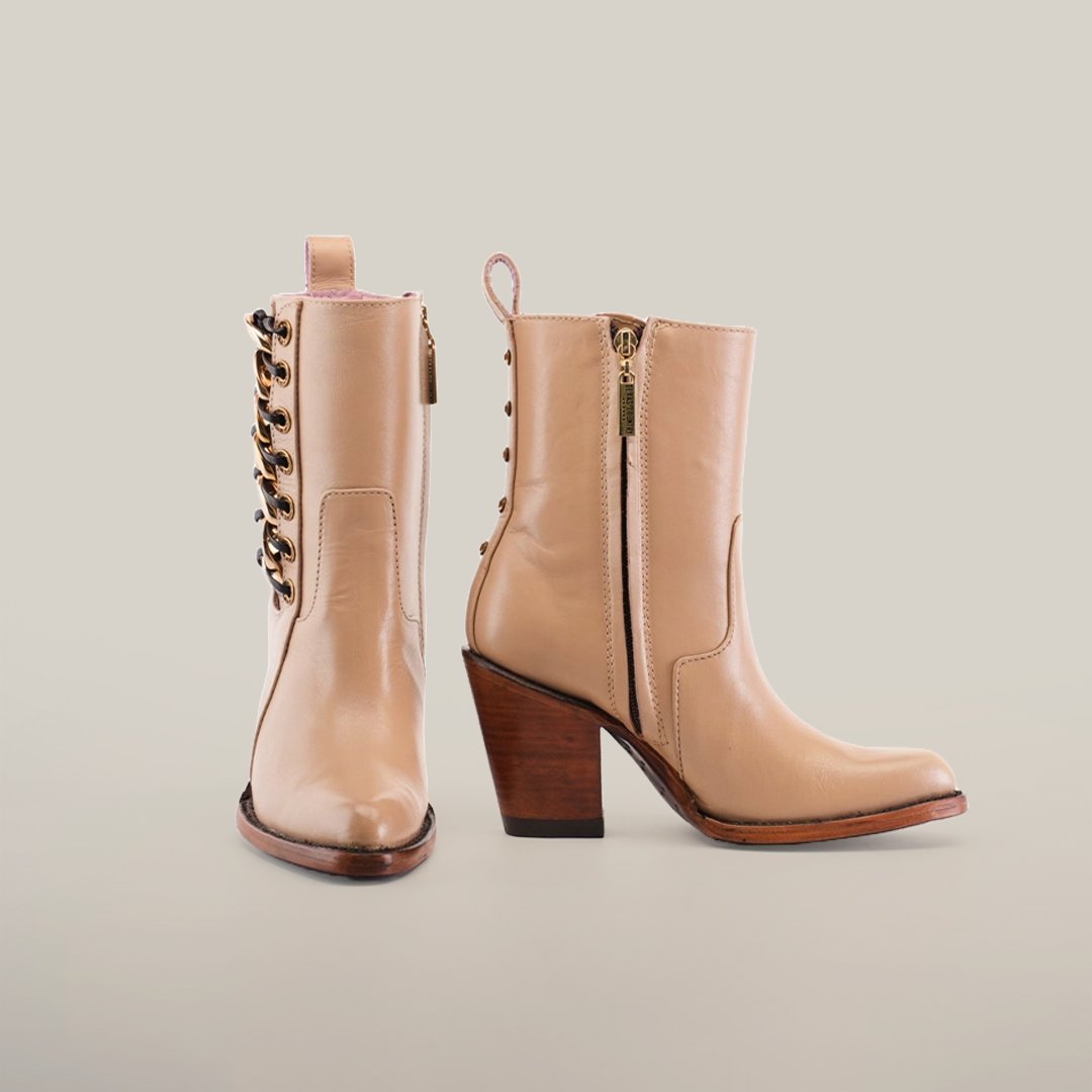 A pair of tan leather boots with medium heels. One boot shows a side zipper, while the other reveals decorative lacing on the side, both resting on a neutral background.