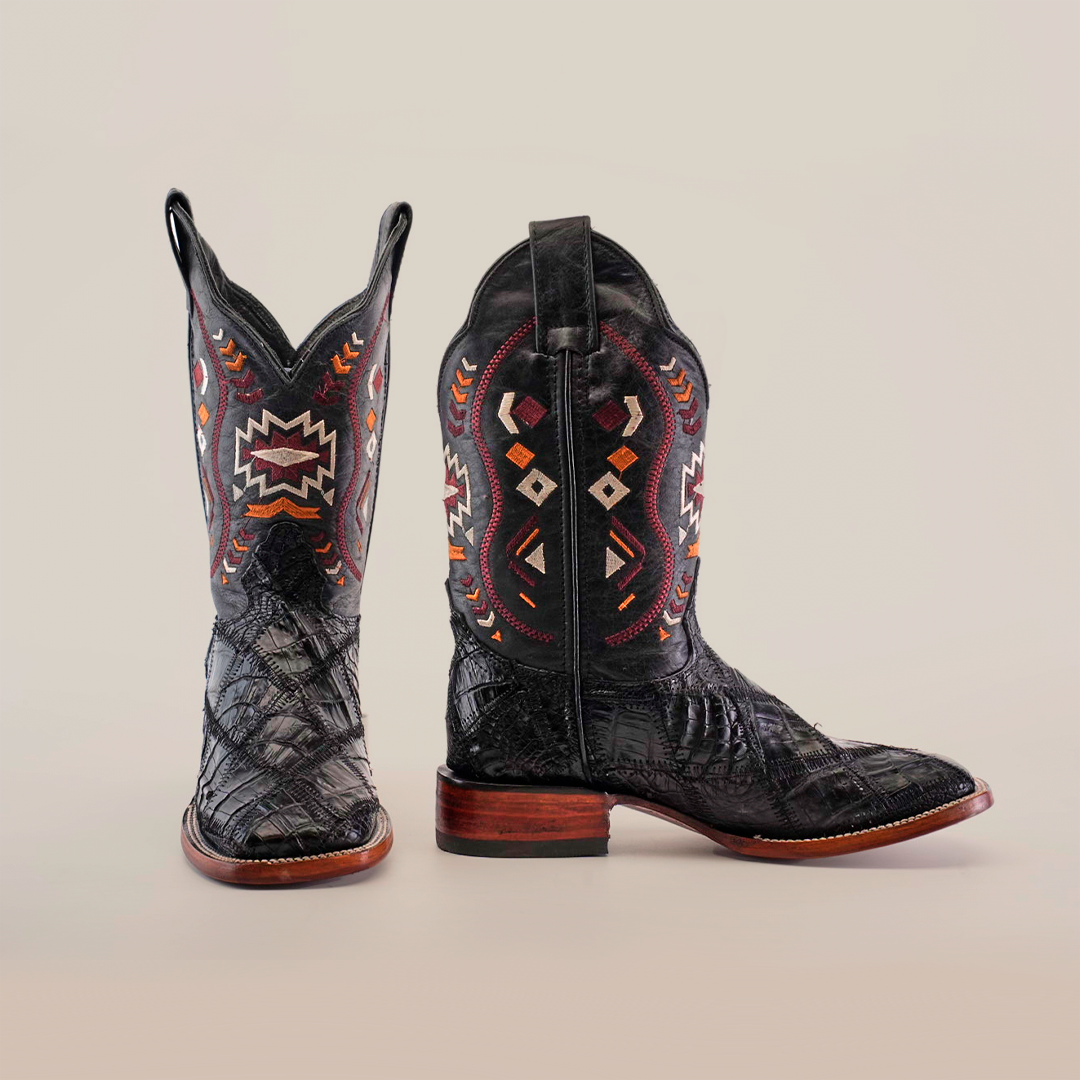 A pair of black cowboy boots with intricate red, white, and orange geometric patterns on the shafts, featuring a textured leather finish and wooden soles, set against a plain background.