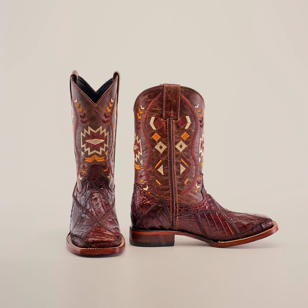 A pair of brown cowboy boots with intricate orange, yellow, and white geometric patterns on the shafts, displayed against a plain background. One boot stands upright, and the other lies on its side.