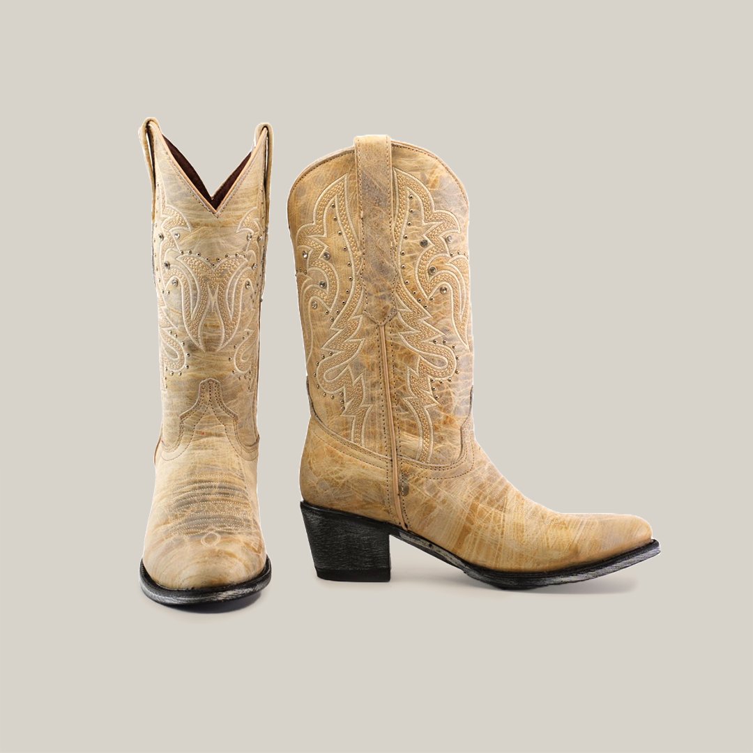 A pair of light brown cowboy boots with intricate embroidery, one boot facing forward and the other facing sideways, set against a plain gray background.