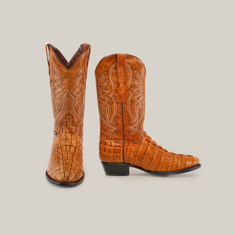 The Crocodile Tail Print Buttercup - Round Toe boots boast premium brown leather with intricate stitching and a textured, crocodile tail pattern. One boot faces forward, while the other showcases its low heel and genuine leather sole against a white background.