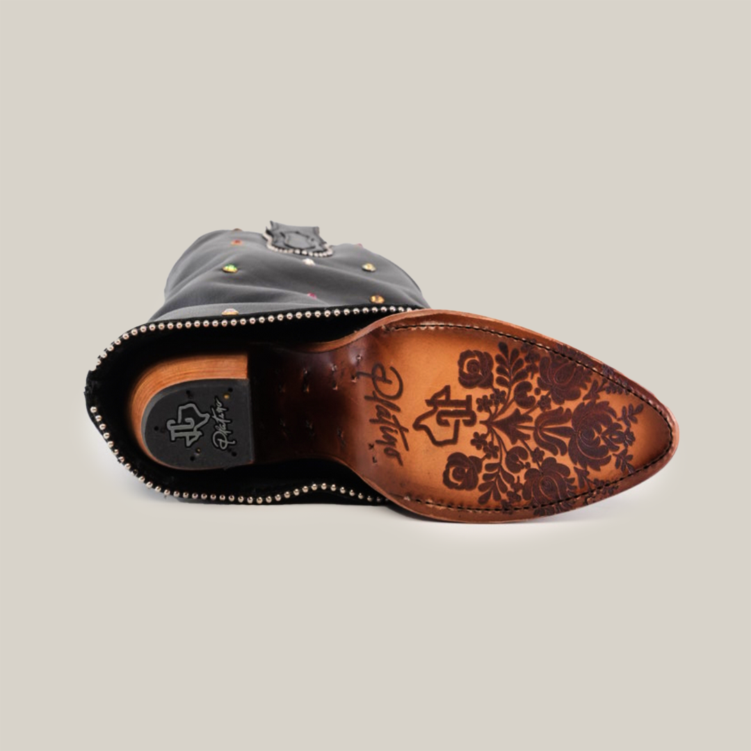 The Roma Rainbow Crystals Tall Shaft Black - J Toe shoe lies on its side, revealing a sole with intricate floral engravings and the brand logo. As part of the Platinum Collection, it boasts metal studs along the edge and a decorative top detail, epitomizing handcrafted treasures.