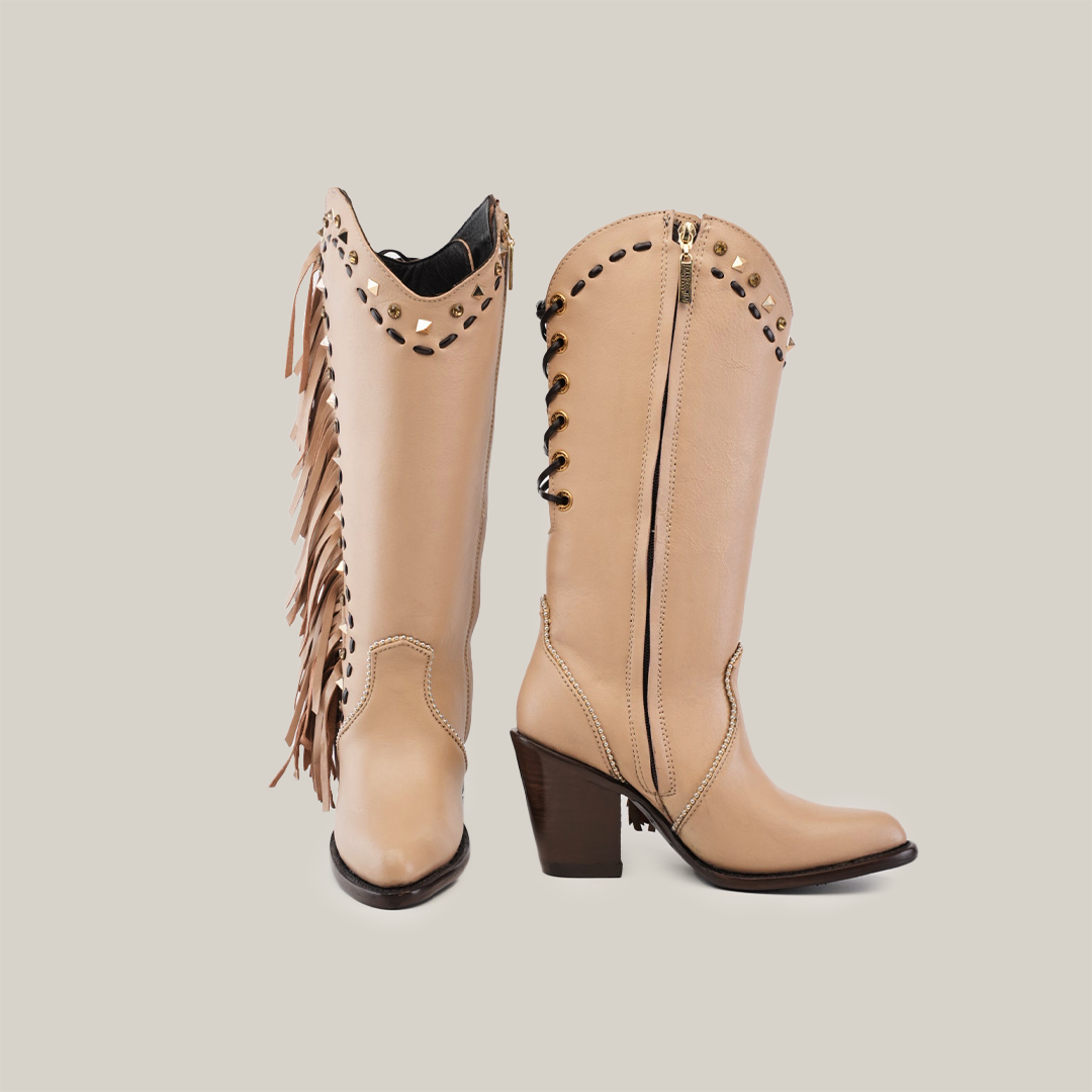 The Praga Fringe Tall Shaft Cream - J Toe boots from our Platinum Collection are handcrafted with tan leather, intricate cut-outs, fringe details, a dark stacked heel, and a zipper, all set against a plain white background.