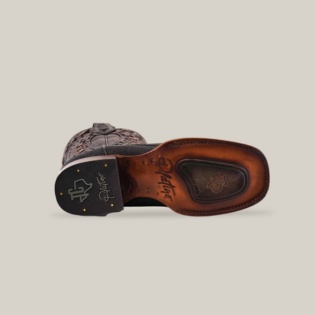 The Exotic Stingray Herradura boot features a bottom view with intricate stitching on the brown leather sole and heel. Its Goodyear welt sole has embossed logos in dark and light brown tones, while a black pattern near the top highlights its elegant design.