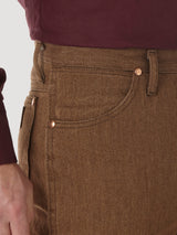 A person in Wrangler Cowboy Cut Slim Fit Jean - 100936BKW, featuring brown fabric with copper rivets, is wearing a maroon shirt. The focus is on the waistband and pocket, highlighting the relaxed fit as a hand rests on the side.