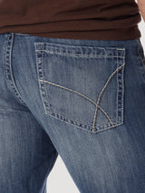 Close-up of a person in a plain, light-colored setting wearing brown shirt and Mens Wrangler 20X No. 42 Vintage Bootcut Jean - 1042MWXLB, featuring detailed back pocket stitching.