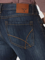 Close-up of premium denim blue jeans with tan stitching and distinct angular pockets, featuring a leather patch with a bulls head logo. The classic design of Wrangler® 20X® No. 42 - Vintage Boot Jean 1042MWXRD stands out against a plain white background.