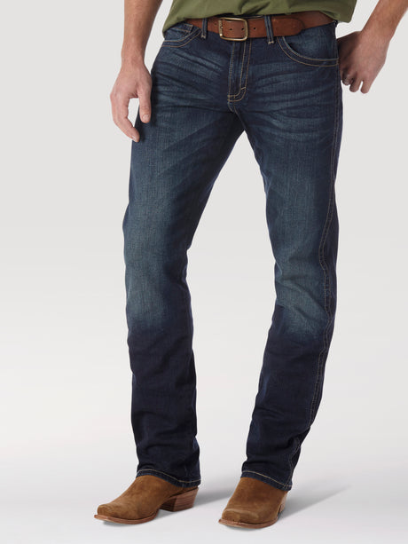 A person in Mens Wrangler 20X No. 42 Vintage Bootcut Jeans and brown boots stands against a plain background, featuring faded premium denim and a sleek brown leather belt, with their top part not visible.