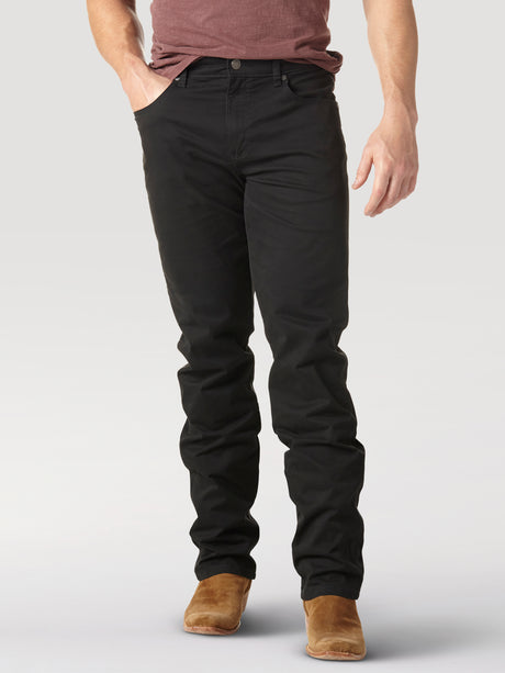 Sporting a maroon shirt, Mens Wrangler Retro Slim Fit Straight Leg Pant in black, and brown shoes, a person stands casually with hands in pockets against a minimalist background. The cropped image highlights the casual sophistication of premium denim.