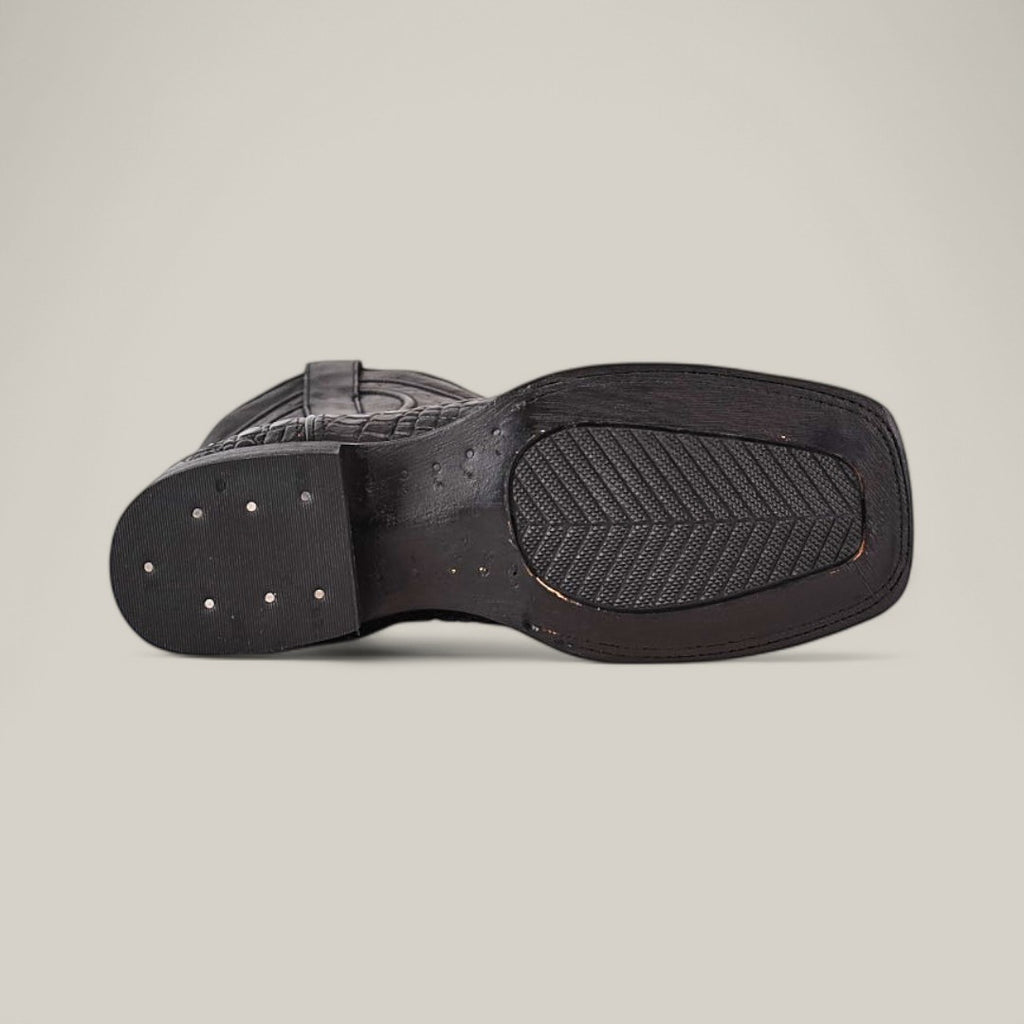 The bottom view of the Alligatoar Horn Back Print Black - Square Toe boot highlights textured leather craftsmanship. Its rectangular sole has a ribbed grip with metal studs on the heel, enhancing its sleek style against a plain light grey background.