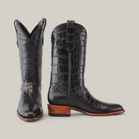 The Exotic Full American Alligator - Black - Round Toe boots are made from premium alligator leather with a shiny, textured pattern. These luxurious cowboy boots have classic features set against a plain gray background.