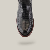 A black, glossy Exotic Full American Alligator shoe with a crocodile texture and brown sole is shown vertically against a plain, light gray background.