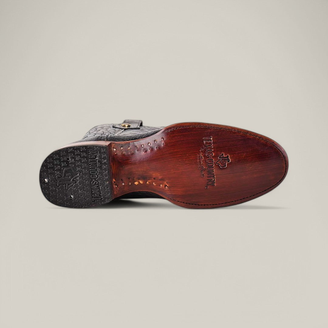 Bottom view of the Exotic Full American Alligator - Black - Round Toe dress shoe, showcasing a brown leather sole with engraved text and logos. The black heel features a textured pattern and logo detailing, epitomizing premium sophistication against a plain, light background.