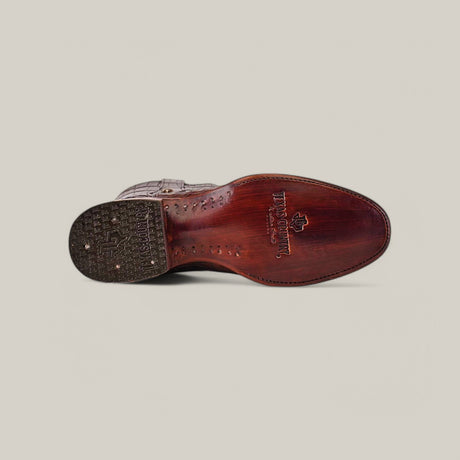 Bottom view of a luxury dress shoe featuring a wooden sole with intricate detailing, including HANDMADE and a decorative pattern. The heel has textured rubber grip and star symbol, similar to American Alligator boots. Shot against a plain, light-colored background. Product: Exotic Full American Alligator - Brown - Round Toe.