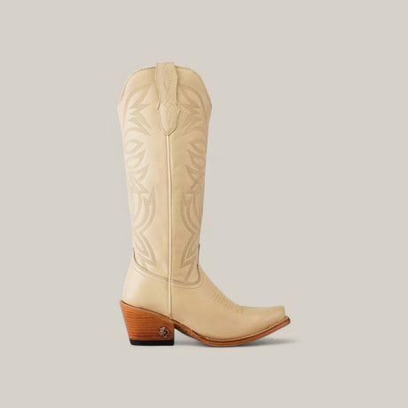 The Kellie Bone Leather Sole boot showcases a side profile view with a tan color, intricate stitching along the tall shaft, a snip toe design, and a wooden block heel against a plain light gray backdrop.