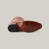 A Miranda Clayton snip toe boot rests on its side, displaying a detailed leather pattern on the shaft and a rich brown leather sole engraved with text and a logo, adorned with metal tacks by the heel against a plain background.