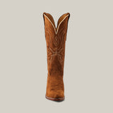 The Miranda Suede Caramel boot features a single tan design with intricate white stitching on the shaft, set against a plain grey backdrop. It has a snip toe and premium leather sole, showcasing luxury craftsmanship.