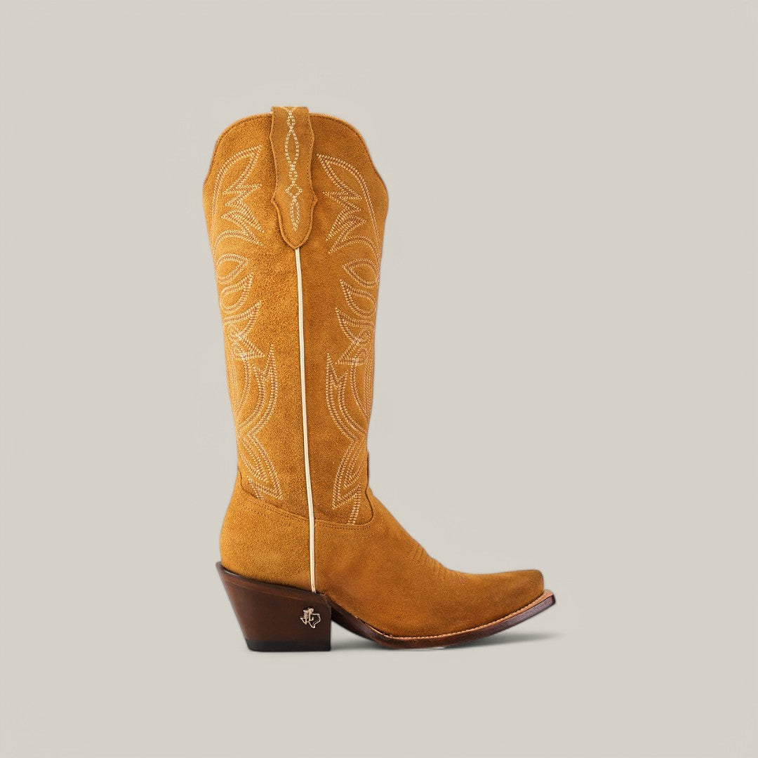 Featuring a stylish brown cowboy boot with a snip toe, this single piece is made from premium suede. It showcases elegant white stitching and has a medium stacked wooden heel and decorative pull straps, reminiscent of the Kellie Suede Gold Lether Sole boots against a gray backdrop.