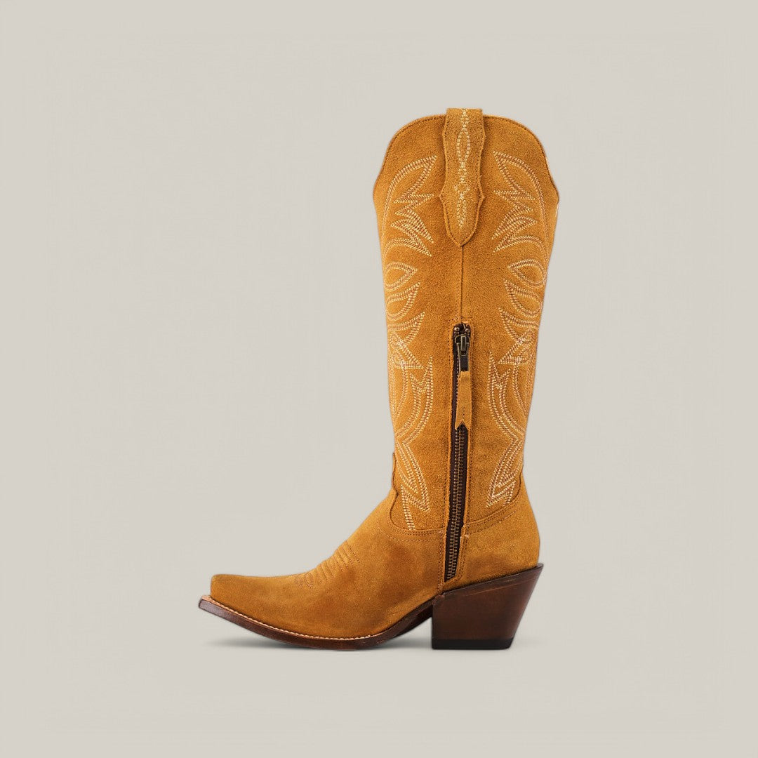 The Kellie Suede Gold Leather Sole boots feature a sophisticated snip toe and decorative shaft stitching. With a side zipper, these tan suede cowboy boots pair premium suede with a stacked wooden heel against a plain beige background for timeless elegance.