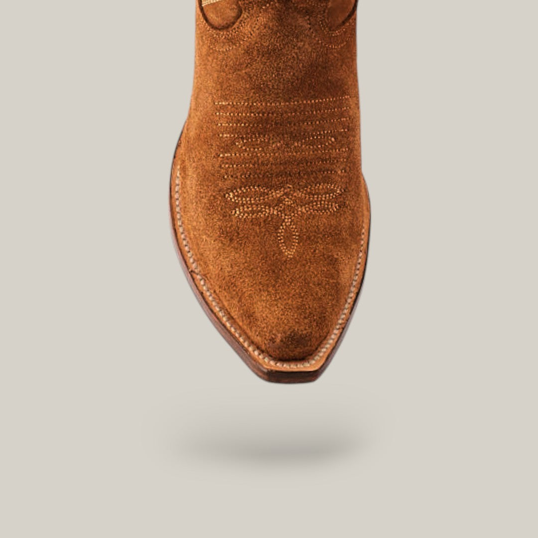 A close-up of the Kellie Suede Caramel Leather Sole boot highlights its snip toe design and intricate stitching. The tall-shaft cowboy boot is showcased against a simple beige background.