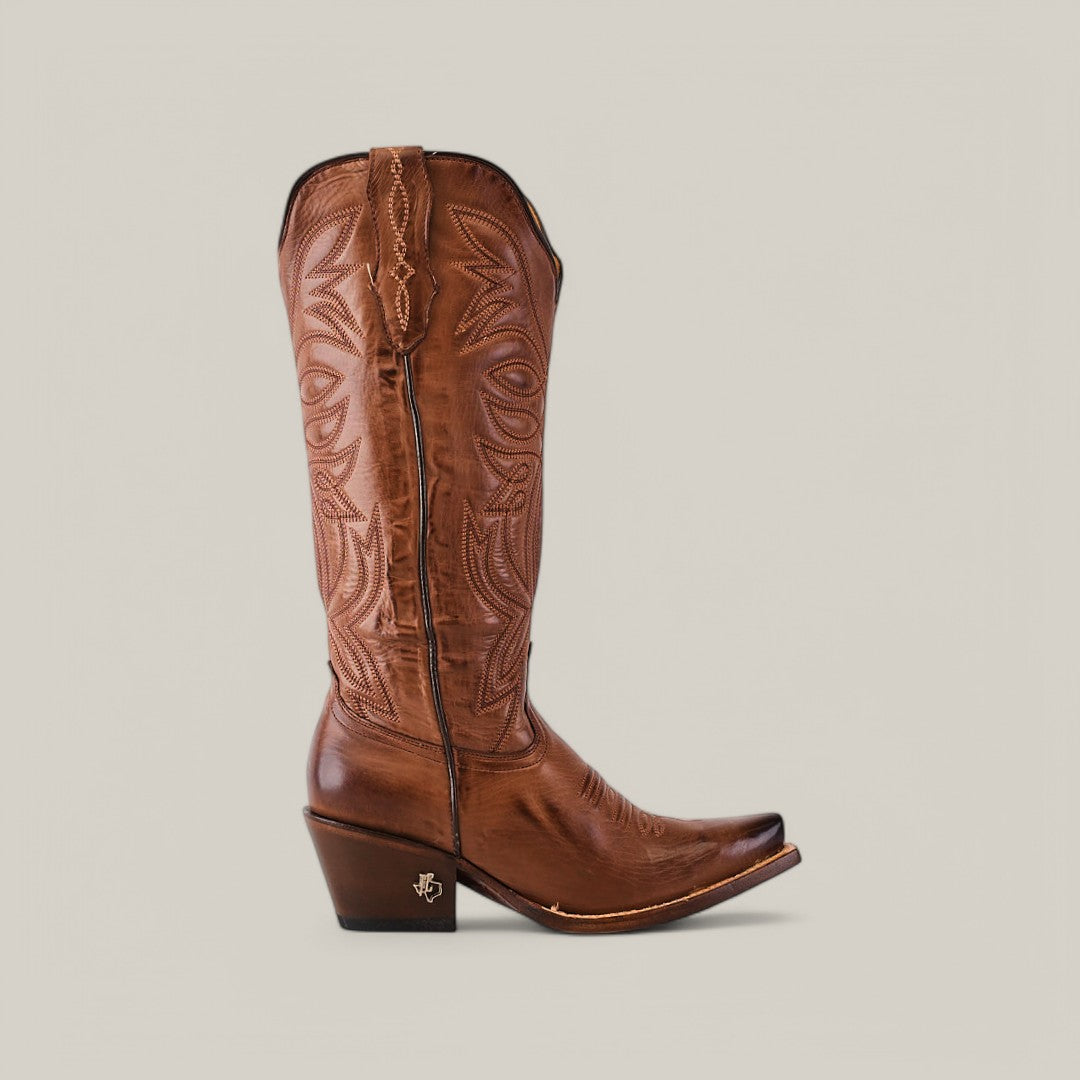 The Kellie Clayton Brown Leather Sole boot exudes Western elegance with intricate embroidery, a snip toe, angled heel, and tall shaft featuring decorative stitching against a plain grey background.