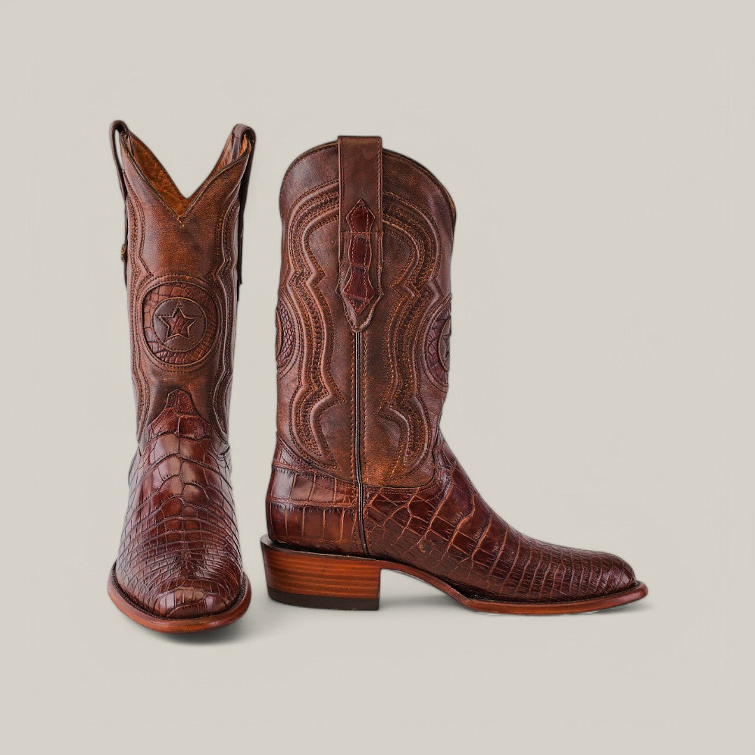 The Exotic American Alligator Belly boots in brown showcase intricate stitching, star detailing, and a stylish roper toe design with one boot upright and the other slightly tilted.