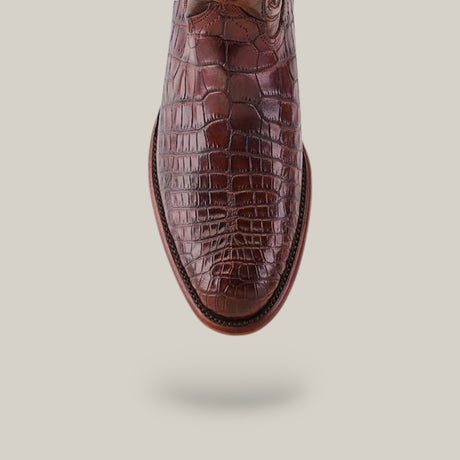 Top view of Exotic American Alligator Belly shoe in brown with a roper toe and detailed stitching, on a neutral background. The texture mimics crocodile skin, and the polished shoe appears to be floating.