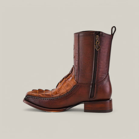 The Exotic American Alligator Tail boots in fawn highlight an alligator leather texture and feature a side zipper. These handcrafted boots boast a narrow square toe, decorative stitching, and a short heel against a plain backdrop.