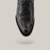 A close-up of the Exotic American Alligator - Europe Black - Round Toe shoe reveals a glossy, high-end alligator leather texture with dark brown stitching, showcasing European design elegance against a light beige background.